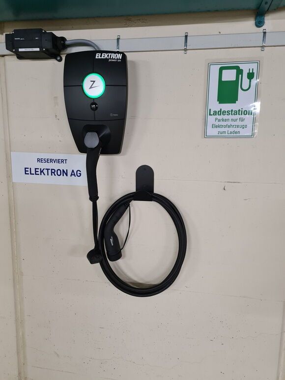 Sort Zaptec ladestation til elbiler med opladningskabel på en lys væg i en parkeringskælder.